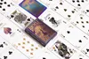 A deck of Bicycle playing cards with a purple and gold peacock design is laid out on a white surface, surrounded by other playing cards. Produktbild-Vorschau