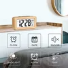 A digital alarm clock with a wooden frame is displayed on a shelf above a bed, with icons and text below highlighting its features. Produktbild-Vorschau