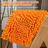 A close-up of an orange chenille mop head resting on a wooden surface, with text overlays describing its features. Produktbild-Vorschau