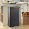A black trash can with two compartments is shown in a kitchen setting, next to a grocery bag filled with produce. Podgląd zdjęcia produktu