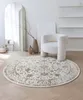 A round rug with an oriental pattern is placed on a wooden floor in a minimalist living room setting, next to a plush armchair and decorative vases. Náhled obrázku produktu