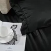 A close-up view of black bedding with a white teacup and saucer placed on an open magazine. Produktbild-Vorschau