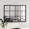 A mirror with a black grid frame is mounted on a white wall. A sofa and a pillow are reflected in the mirror. A plant is in the foreground. Podgląd zdjęcia produktu