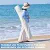 A person walks on a beach carrying a rolled-up cream-colored item. Produktbild-Vorschau