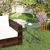 A green round side table with a cup of coffee on it, placed on a lawn next to a brown wicker sofa. Produktbild-Vorschau