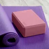 A pink yoga block rests on a rolled-up purple yoga mat, with a wooden floor in the background. Náhled obrázku produktu