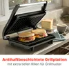 A close-up shot of a black panini grill with two sandwiches being grilled, with a slice of bread and a cup of coffee in the background. Produktbild-Vorschau