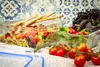 Two glass food storage containers filled with pasta salad and green salad, with cherry tomatoes and breadsticks on a checkered cloth. Produktbild-Vorschau