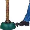 A person's foot is shown stepping on a pedal of a green Christmas tree stand, which holds a tree trunk. Náhľad obrázku produktu