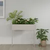A planter with plants and flowers on a stand, next to another potted plant. Produktbild-Vorschau