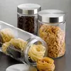 Three glass storage jars with metal lids, two upright and one lying down, filled with coffee beans, cereal, and pasta. Náhled obrázku produktu