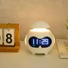 A digital alarm clock with a Bluetooth speaker function is displayed on a white surface next to a wooden calendar. Produktbild-Vorschau