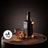 A bottle of Jack Daniel's whiskey and a glass of whiskey with ice are placed on a wooden barrel. Produktbild-Vorschau