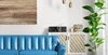 A living room scene with a blue sofa, a cabinet with a radio, and a plant. Produktbild-Vorschau