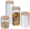 Four glass storage jars with wooden lids are arranged on a white background. One jar contains brown sugar cubes, another contains tri-colored penne pasta, and the other two are empty. Produktbild-Vorschau