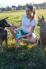 A woman is crouching in a grassy field with two dogs, holding a product box. Produktbild-Vorschau