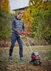 A man is using a tiller in a garden with trees in the background. Produktbild-Vorschau