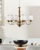 A brass-colored chandelier with six white lampshades hangs above a dining table. Náhled obrázku produktu