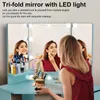A woman is applying makeup in front of a tri-fold mirror with LED lights. Podgląd zdjęcia produktu