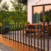 A modern deck with a wooden floor and a black metal railing, leading to a house with a patio and outdoor furniture. Náhľad obrázku produktu