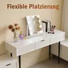 A white vanity table with a lighted makeup mirror, flowers in a vase, and perfume. Náhľad obrázku produktu