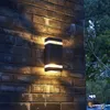 A black LED wall light is mounted on a brick wall at night, with trees visible in the background. Podgląd zdjęcia produktu