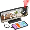 A digital alarm clock with a projected time display and a smartphone charging next to it. Produktbild-Vorschau