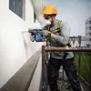 A construction worker is drilling into a wall while standing on scaffolding. Produktbild-Vorschau