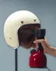 A hand is holding a red steamer to clean the inside of a cream-colored helmet. Anteprima dell’immagine prodotto