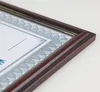 A close-up, angled view of a mahogany-colored picture frame holding a certificate or document. Produktbild-Vorschau