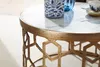 Close-up of a marble-topped coffee table with a gold metal base featuring a geometric pattern. A blue and white patterned vase and a blue glass object are on the table. Produktbild-Vorschau