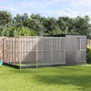 A large aviary structure with a metal frame and mesh walls, attached to a wooden fence, set in a grassy backyard with trees in the background. Produktbild-Vorschau