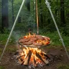 A round metal grill grate with food is suspended over a campfire in a forest setting. Anteprima dell’immagine prodotto