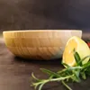 A bamboo salad bowl with a slice of lemon and rosemary in front of it, on a dark background. Produktbild-Vorschau