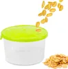 A clear plastic food container with a bright green lid, with cornflakes being poured into it and a pile of cornflakes next to it. Náhled obrázku produktu