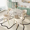 A dining set with a marble-top table and four cream-colored chairs placed on a rug with a black abstract pattern. Náhled obrázku produktu