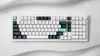 A top-down view of a white mechanical keyboard with dark gray and green keycaps, set against a white and light gray background with soft, wavy textures. Produktbild-Vorschau