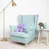 A violet teddy bear sits on a light blue armchair next to a small side table with a plant, a vase, and an alarm clock. Náhľad obrázku produktu