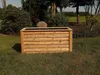 A wooden planter box sits on a grassy lawn in a garden setting, with trees and bushes in the background. Produktbild-Vorschau