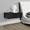 A black floating nightstand with a white lamp and books on it, next to a white tufted headboard. Náhled obrázku produktu