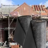 Construction site with scaffolding and building materials, with two rolls of black fabric in the foreground. Podgląd zdjęcia produktu