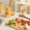 A kitchen counter with pasta jars, tomatoes, basil, garlic, and a wooden spoon. Produktbild-Vorschau