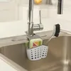 A kitchen sink organizer holding a sponge and a brush next to a faucet. Podgląd zdjęcia produktu