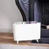 A white magazine rack with magazines inside, placed on a wooden floor next to a fireplace. Podgląd zdjęcia produktu