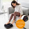 A woman is sitting on a couch and using a foot massager. Produktbild-Vorschau