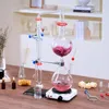 A laboratory distillation setup for essential oils is displayed on a wooden table, with shelves in the background. Produktbild-Vorschau