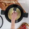 A hand is cleaning a non-stick pan with a sponge, with ingredients like tomatoes and garlic in the background. Náhľad obrázku produktu