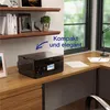 A black printer is placed on a wooden desk next to a window. Náhled obrázku produktu