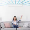 A woman is sitting on a couch and holding a remote control, with an air conditioner unit visible on the wall above her. Produktbild-Vorschau