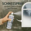 A hand holding a can of snow spray, spraying it onto a window to create a decorative snow effect. Produktbild-Vorschau